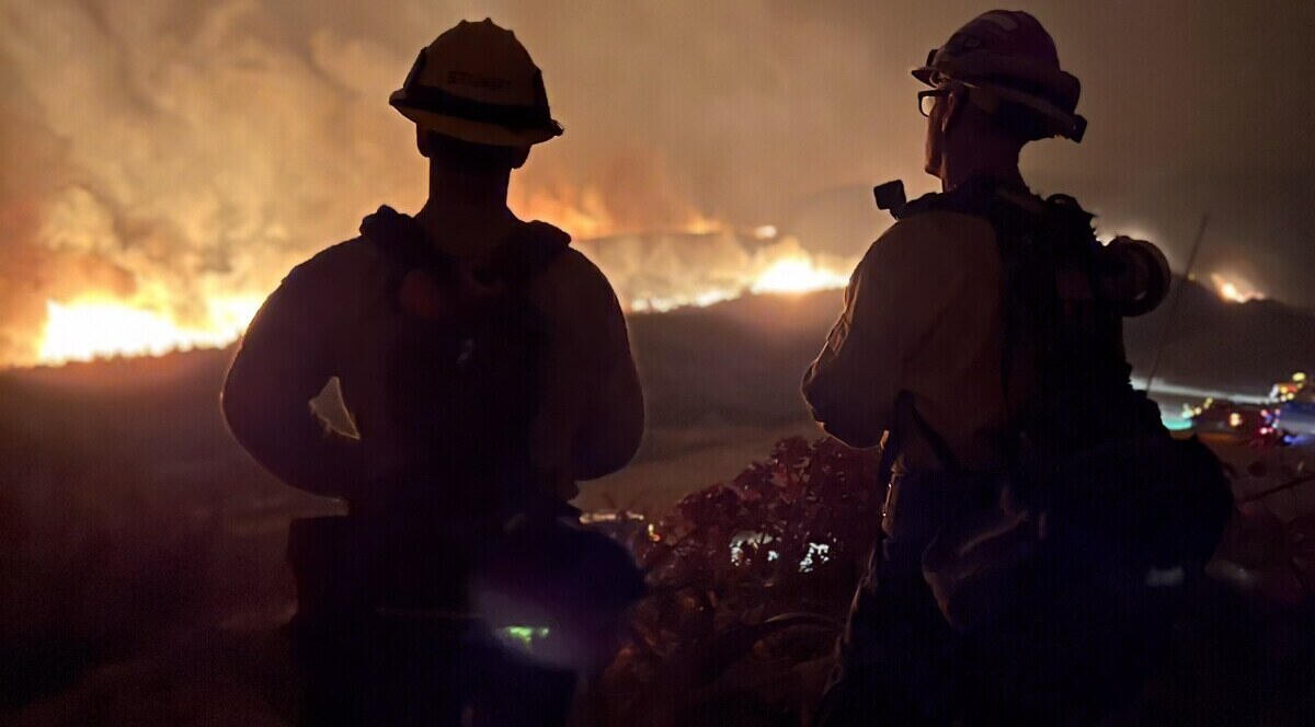 Two firefighters silhouetted against a night wildfire
